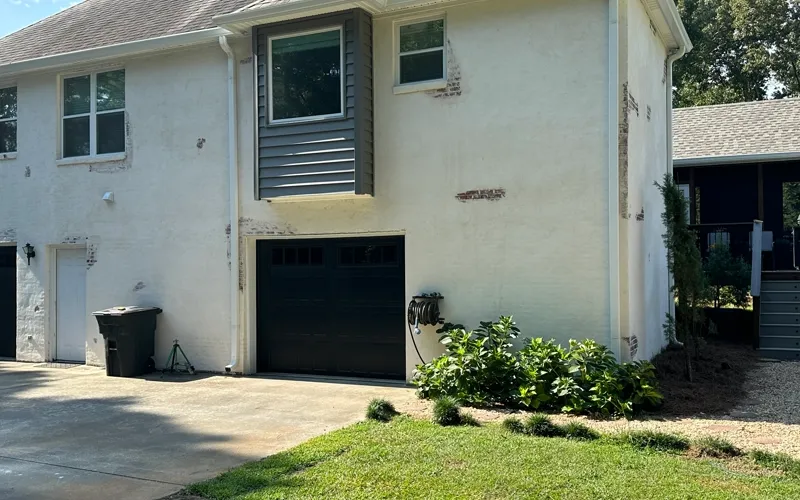 Residential home exterior with fresh white stucco and new black garage door.