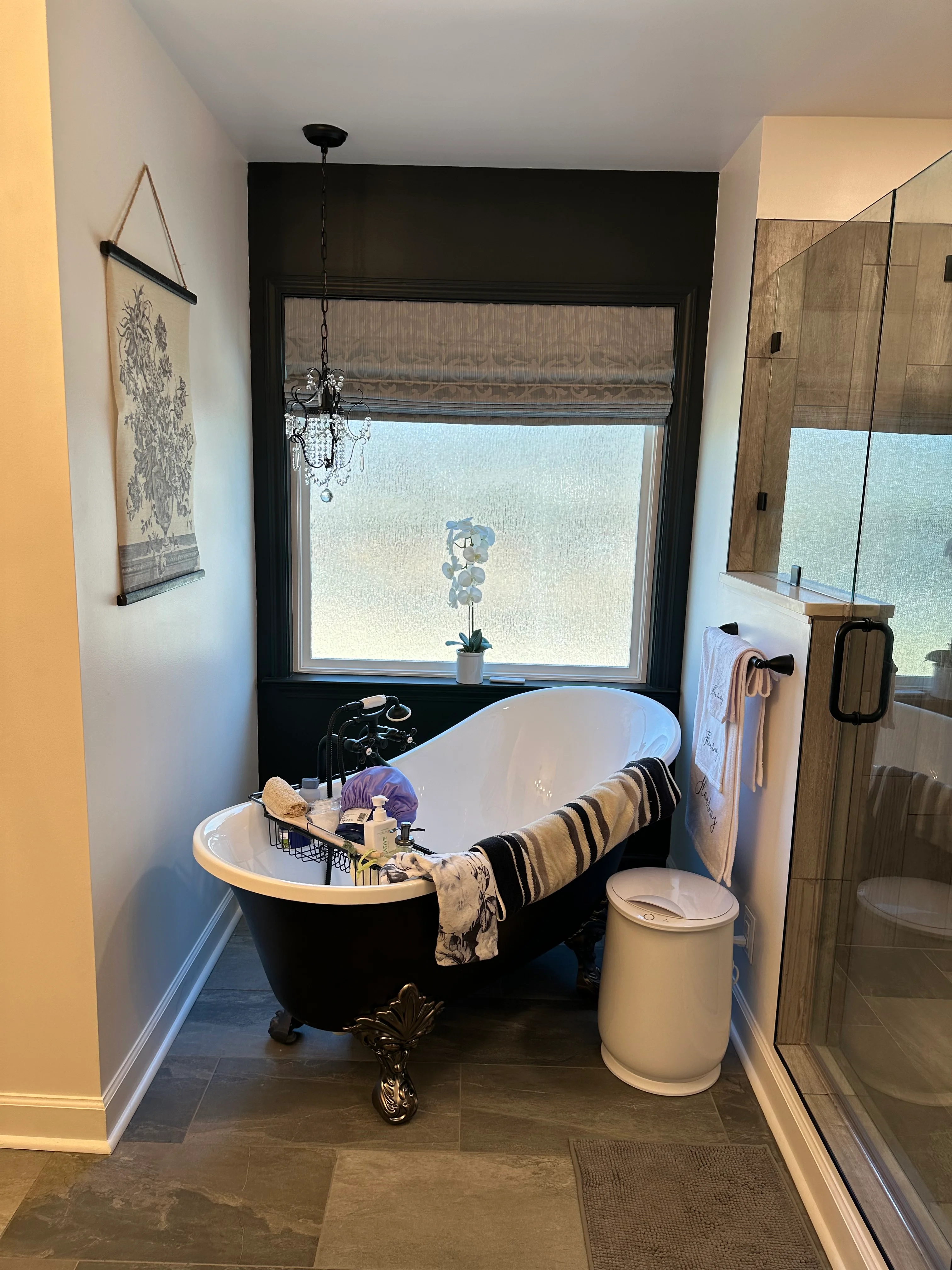 Black freestanding tub with brass feet in renovated bathroom with large window and glass shower