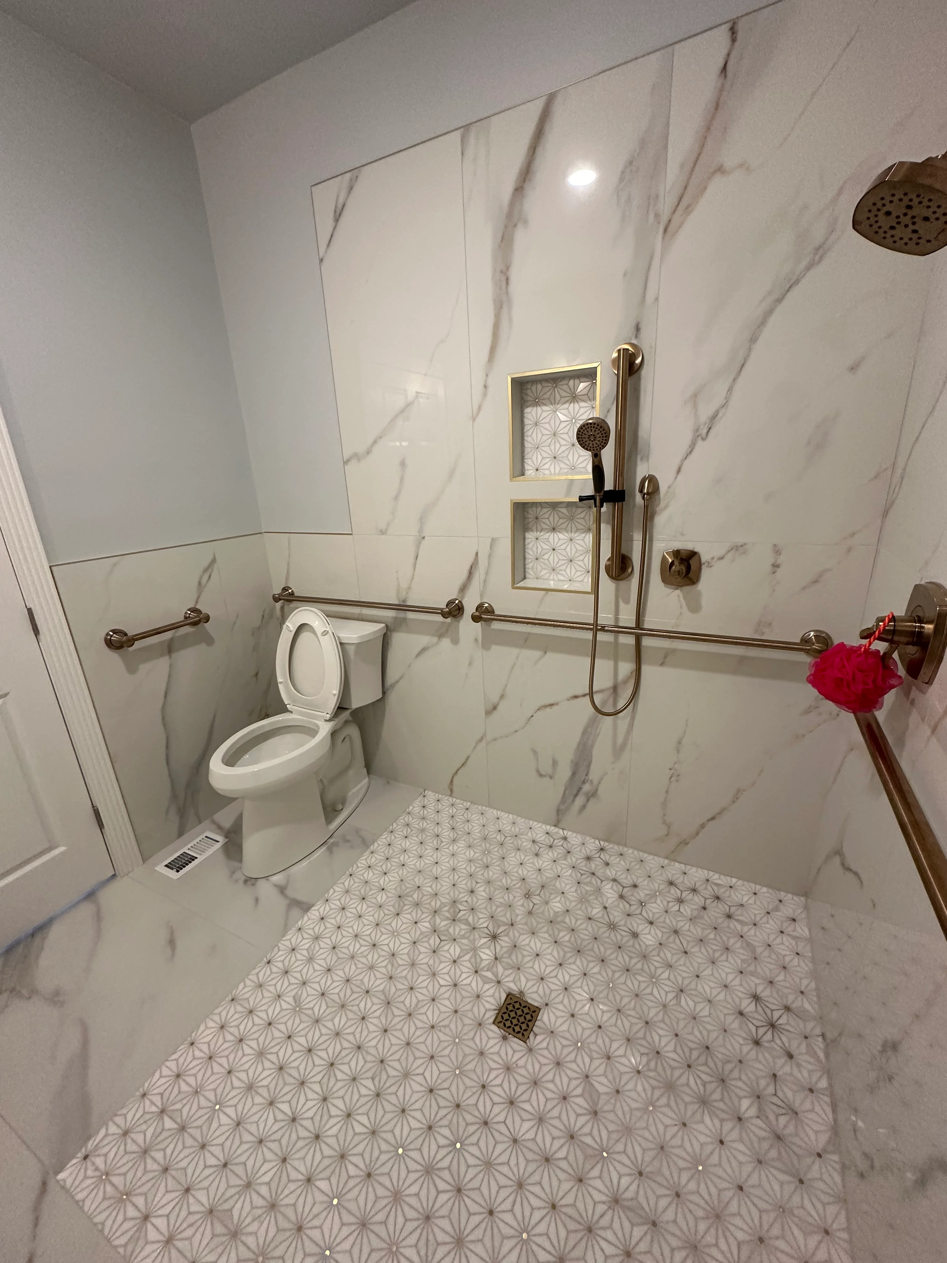 Modern bathroom with marble tile walls, geometric floor tile, and brushed gold fixtures