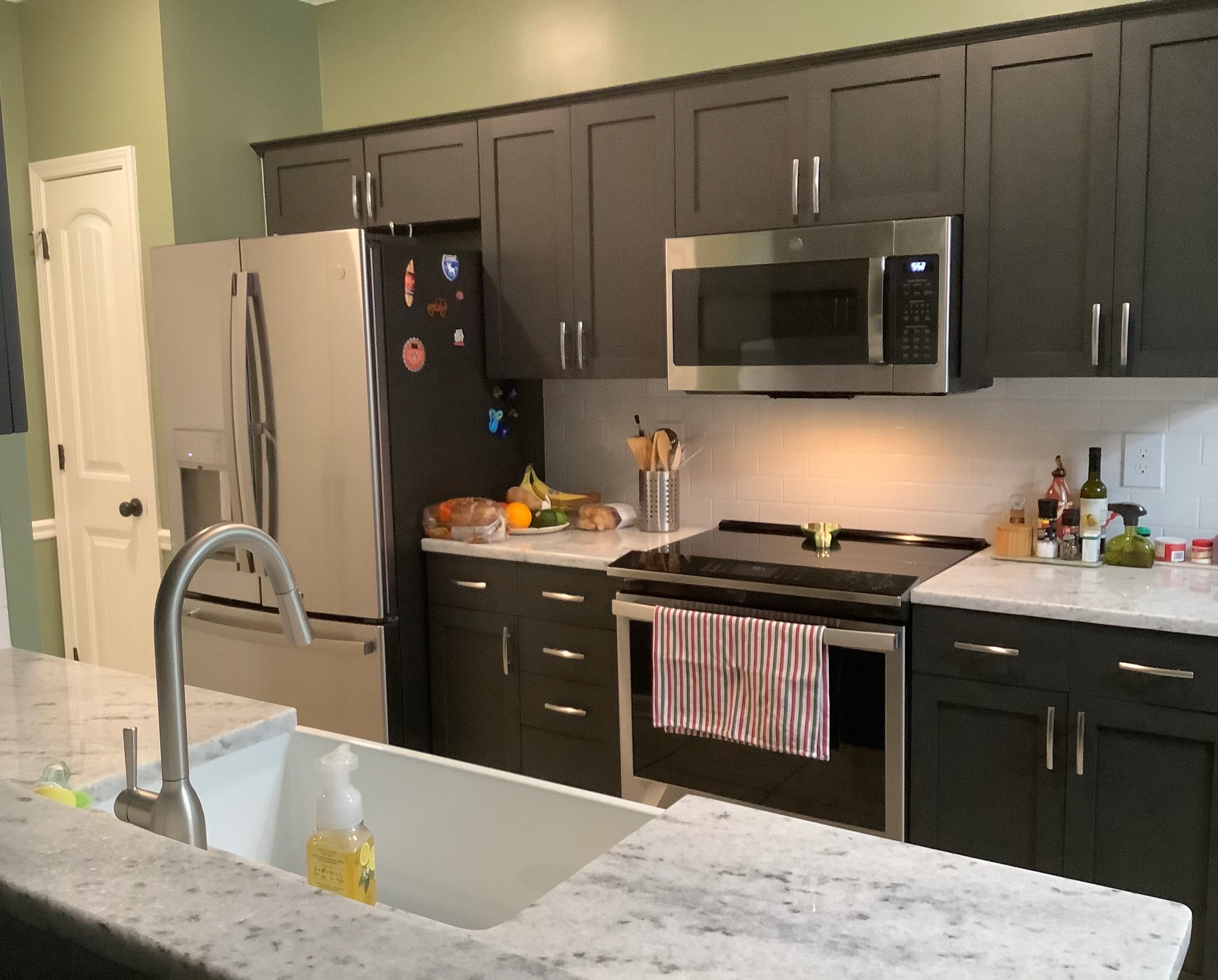 Modern kitchen with dark cabinets, marble counters, stainless steel appliances, and white tile backsplash