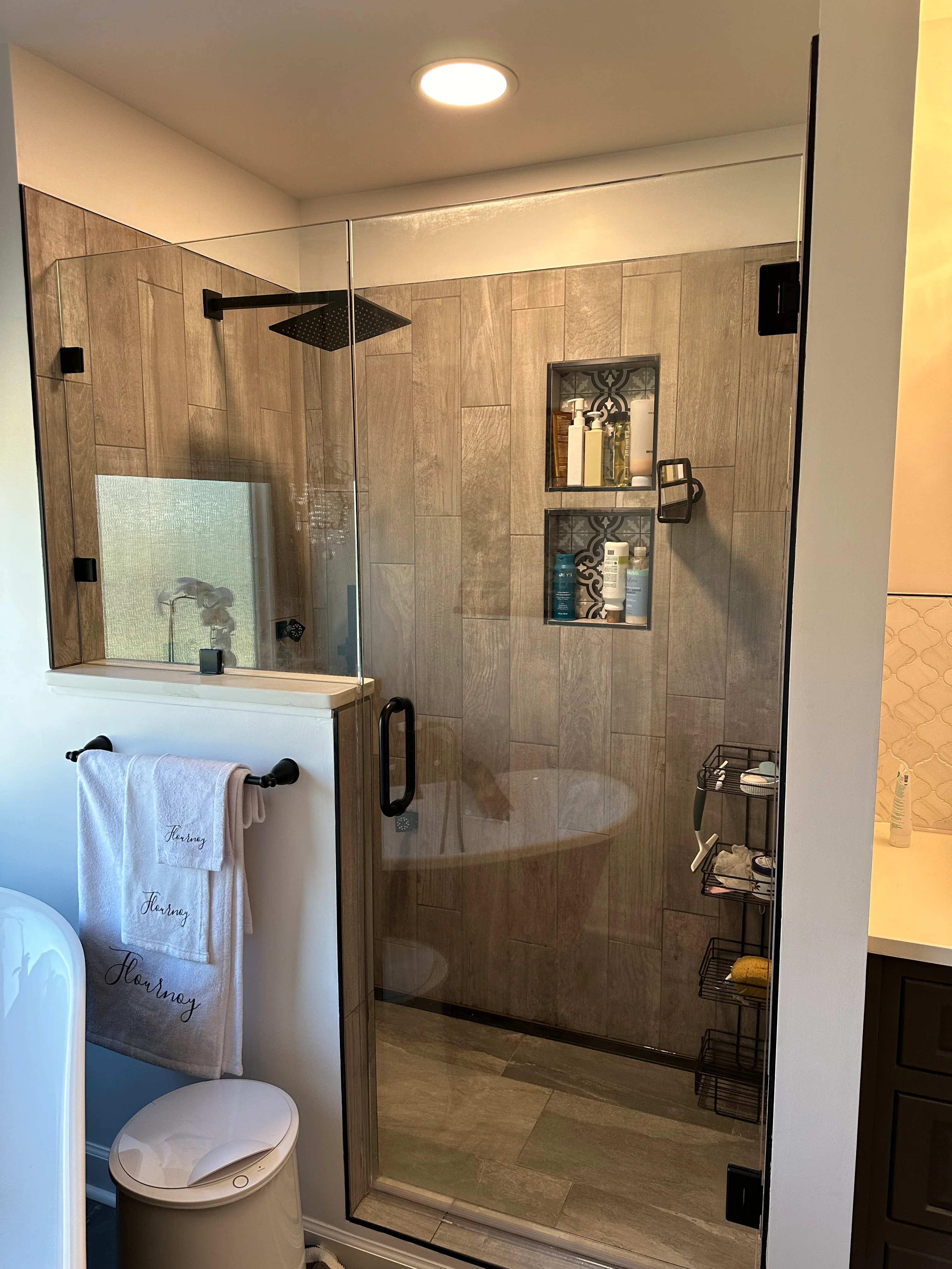Modern walk-in shower with wood-look tile, glass enclosure, and built-in shelving