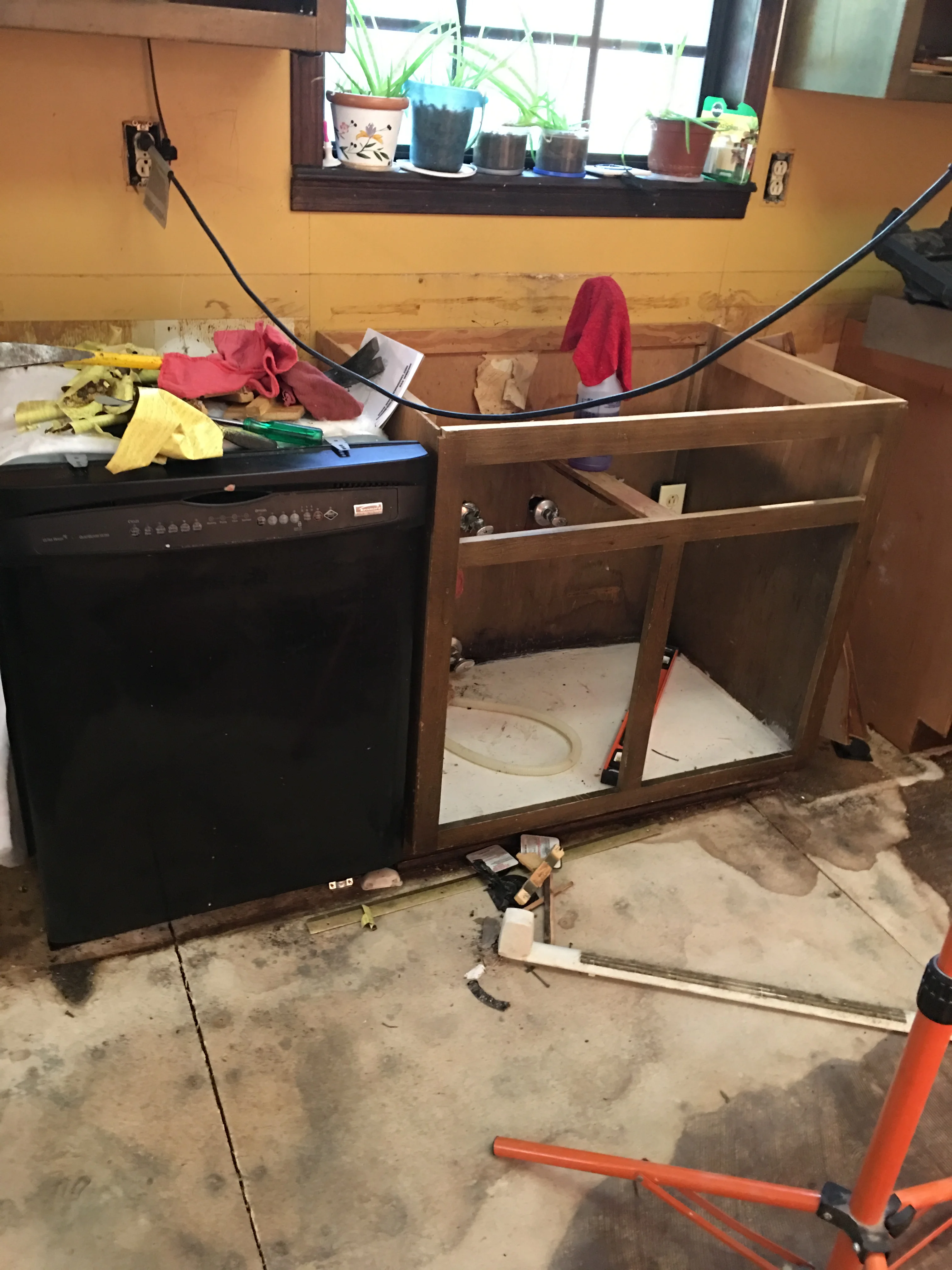 Kitchen remodel in progress showing new wooden cabinetry framing and black dishwasher installation