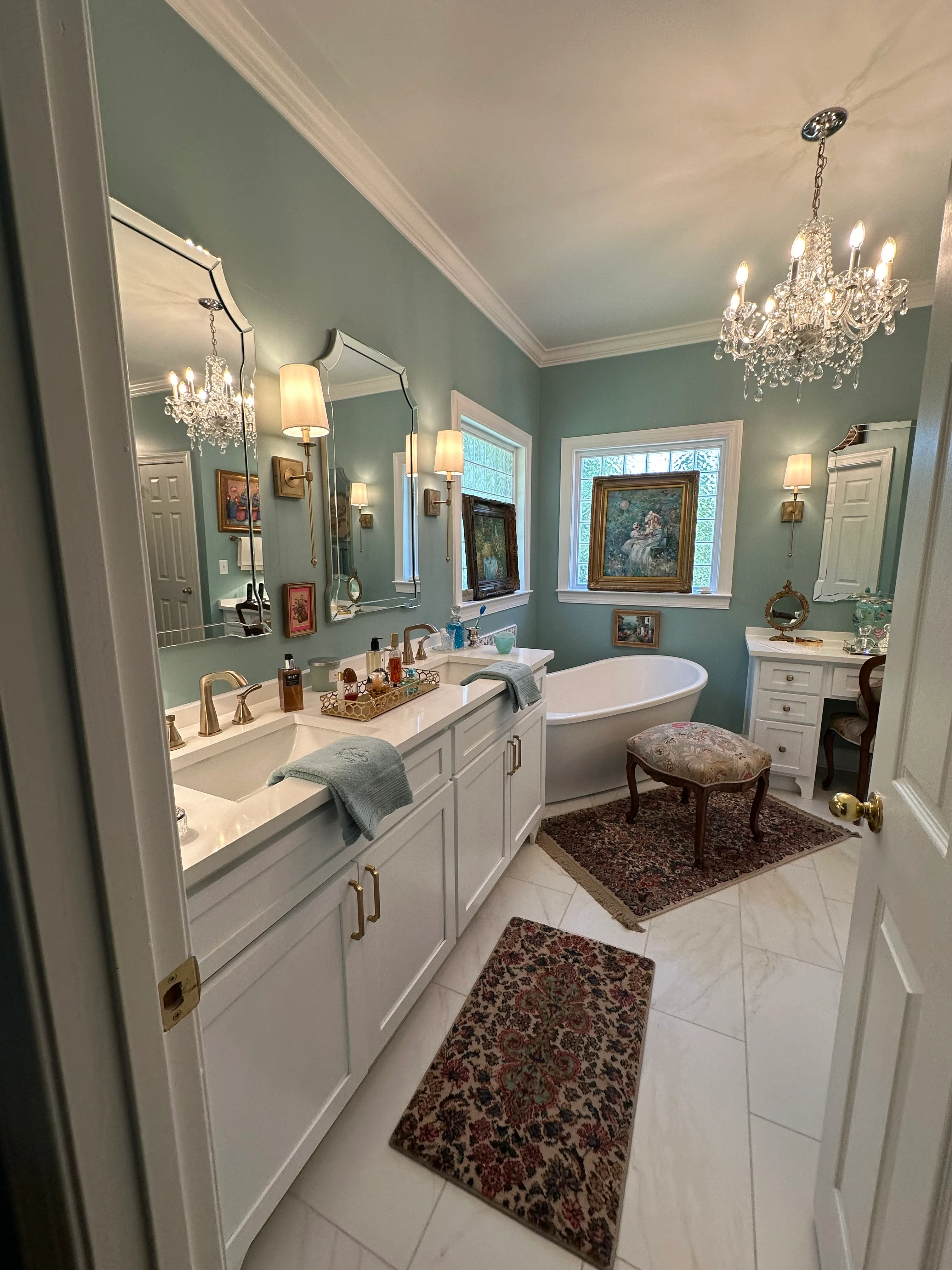 Elegant master bathroom with sage green walls, white vanity, freestanding tub, and crystal chandeliers