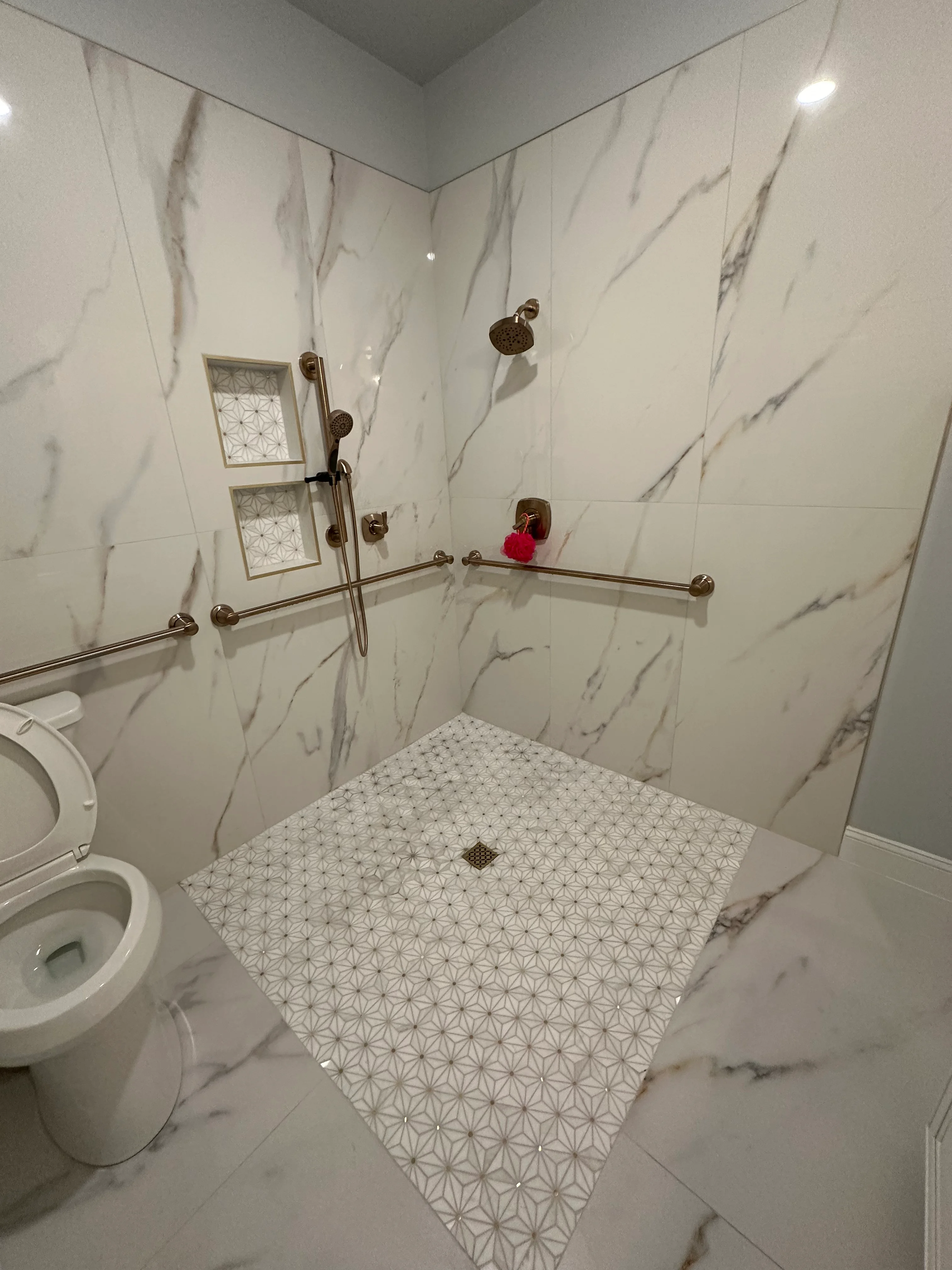 Modern bathroom shower with marble tile walls, geometric floor pattern, and bronze fixtures