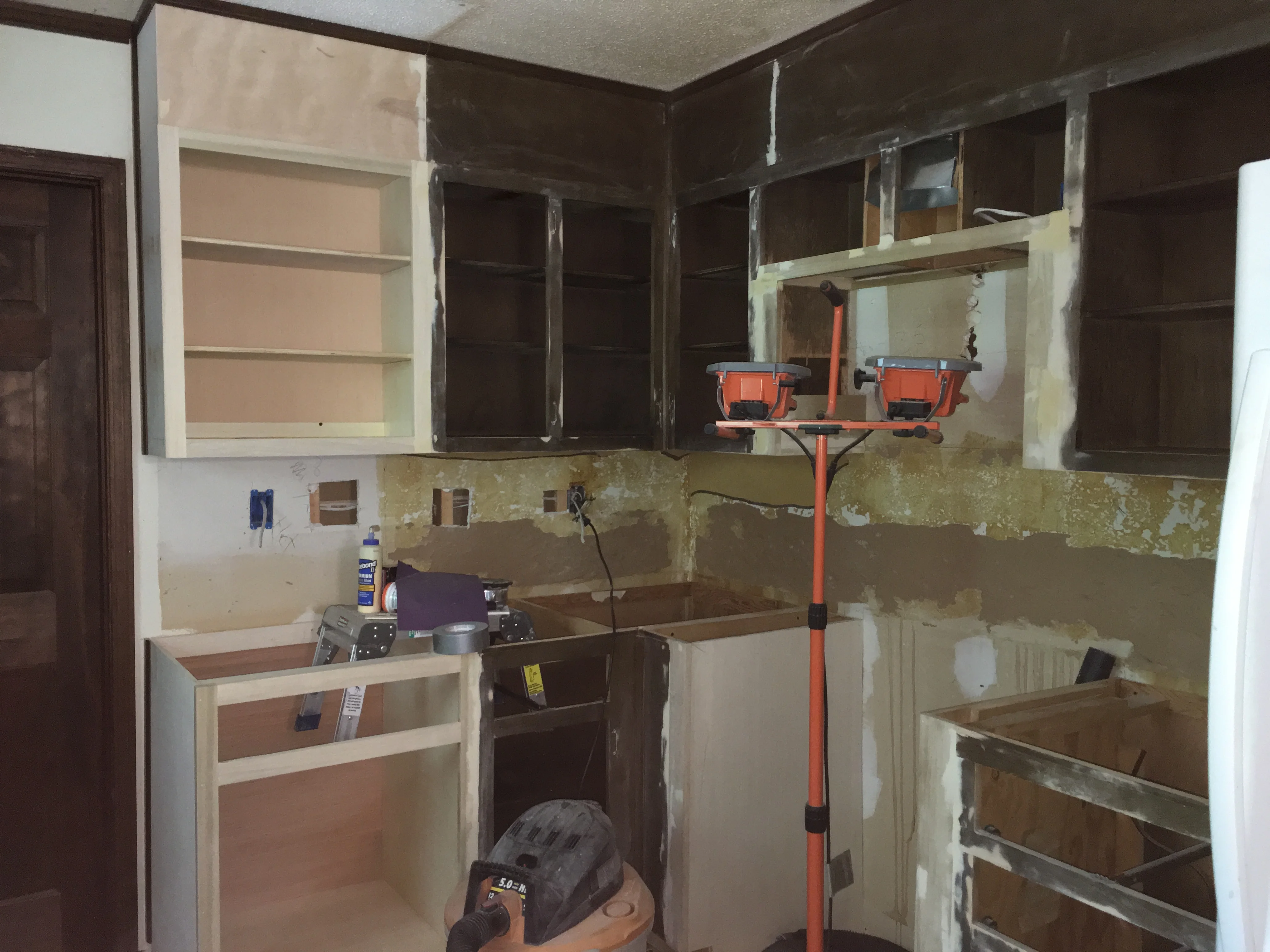 Kitchen remodel in progress with new cabinets, exposed framing, and work lights