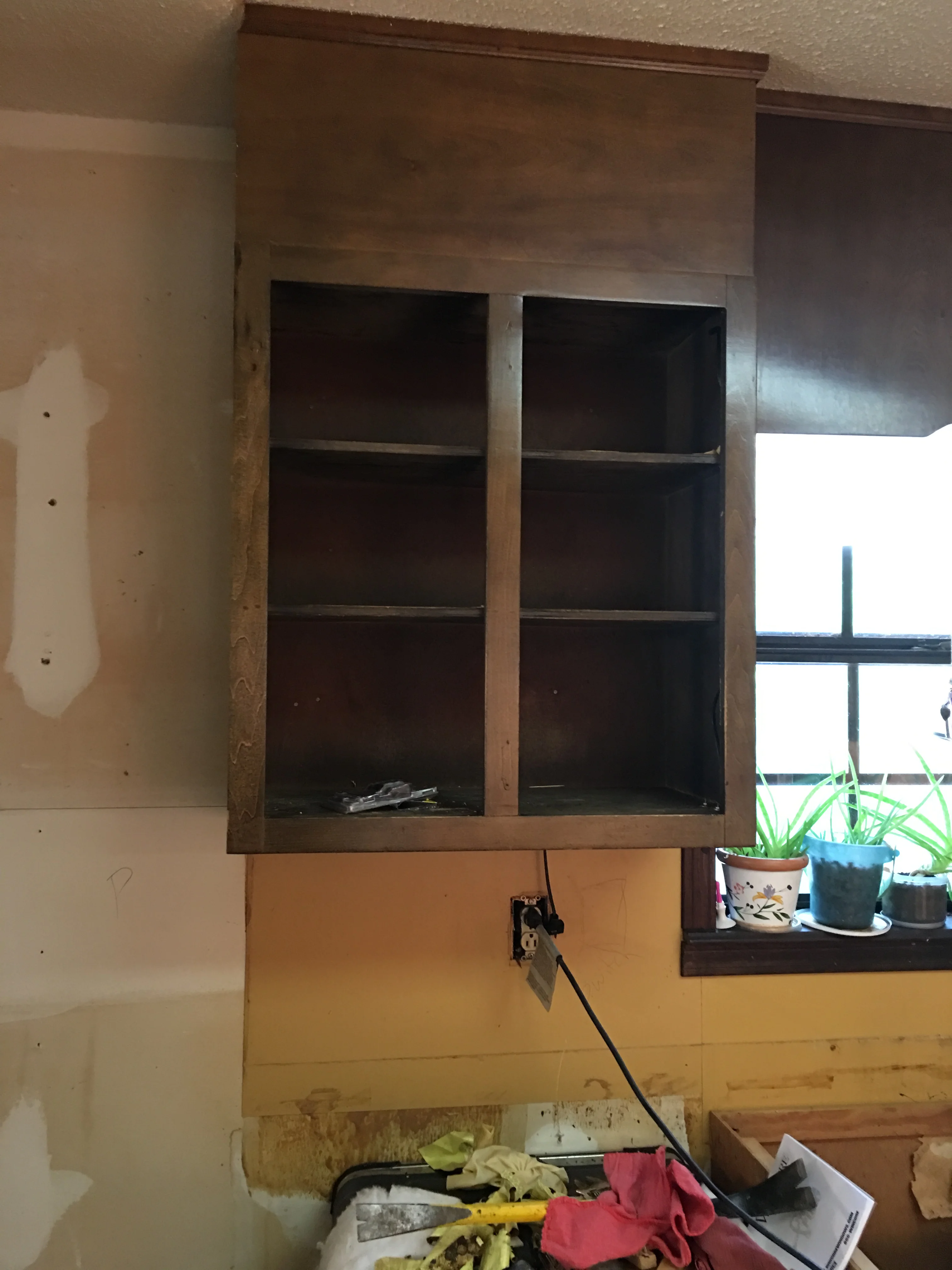 Dark wood cabinet with glass-front doors and three shelves installed above kitchen window