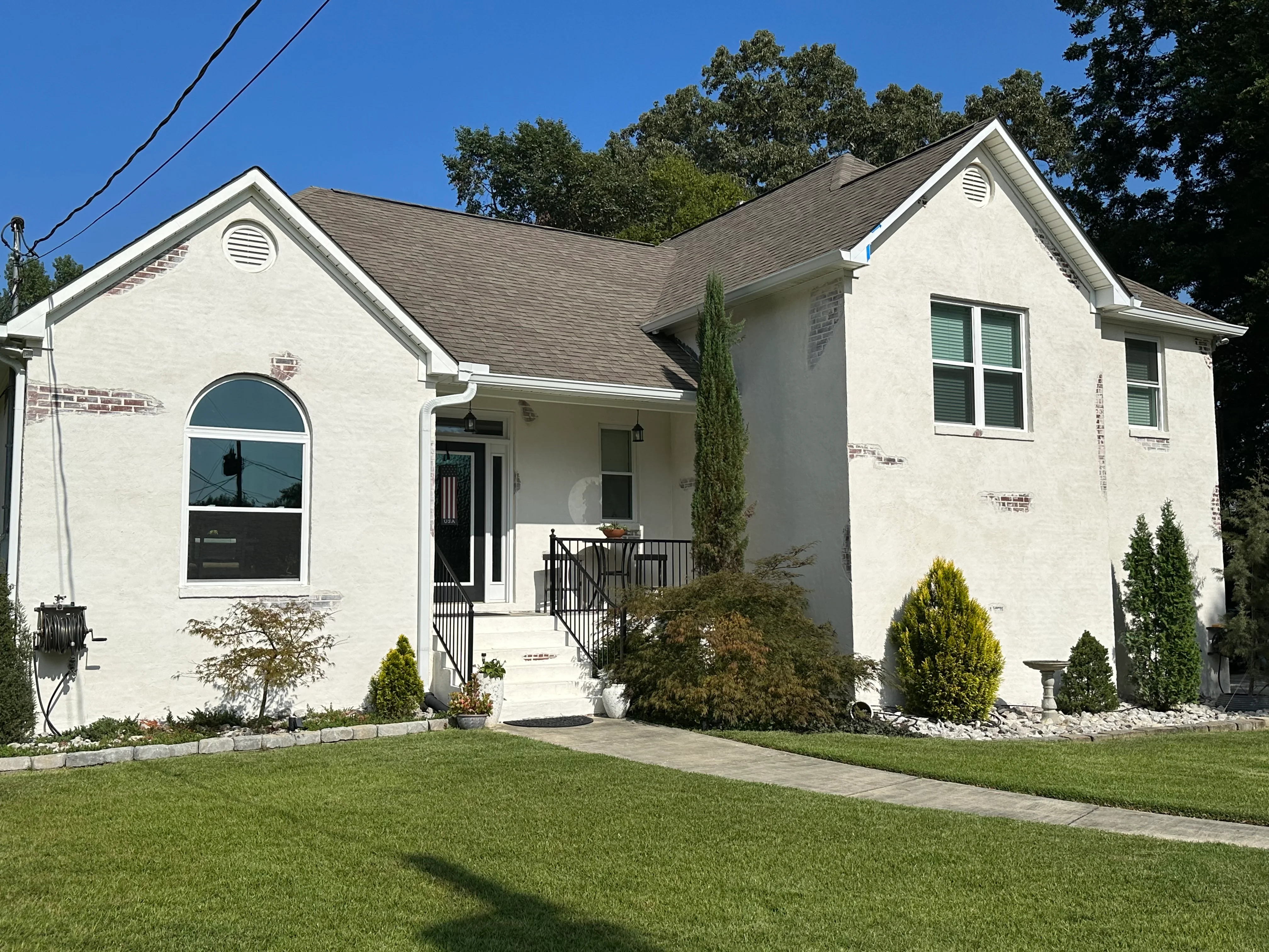 White stucco home with gray roof, new windows, black railings, and landscaped front yard