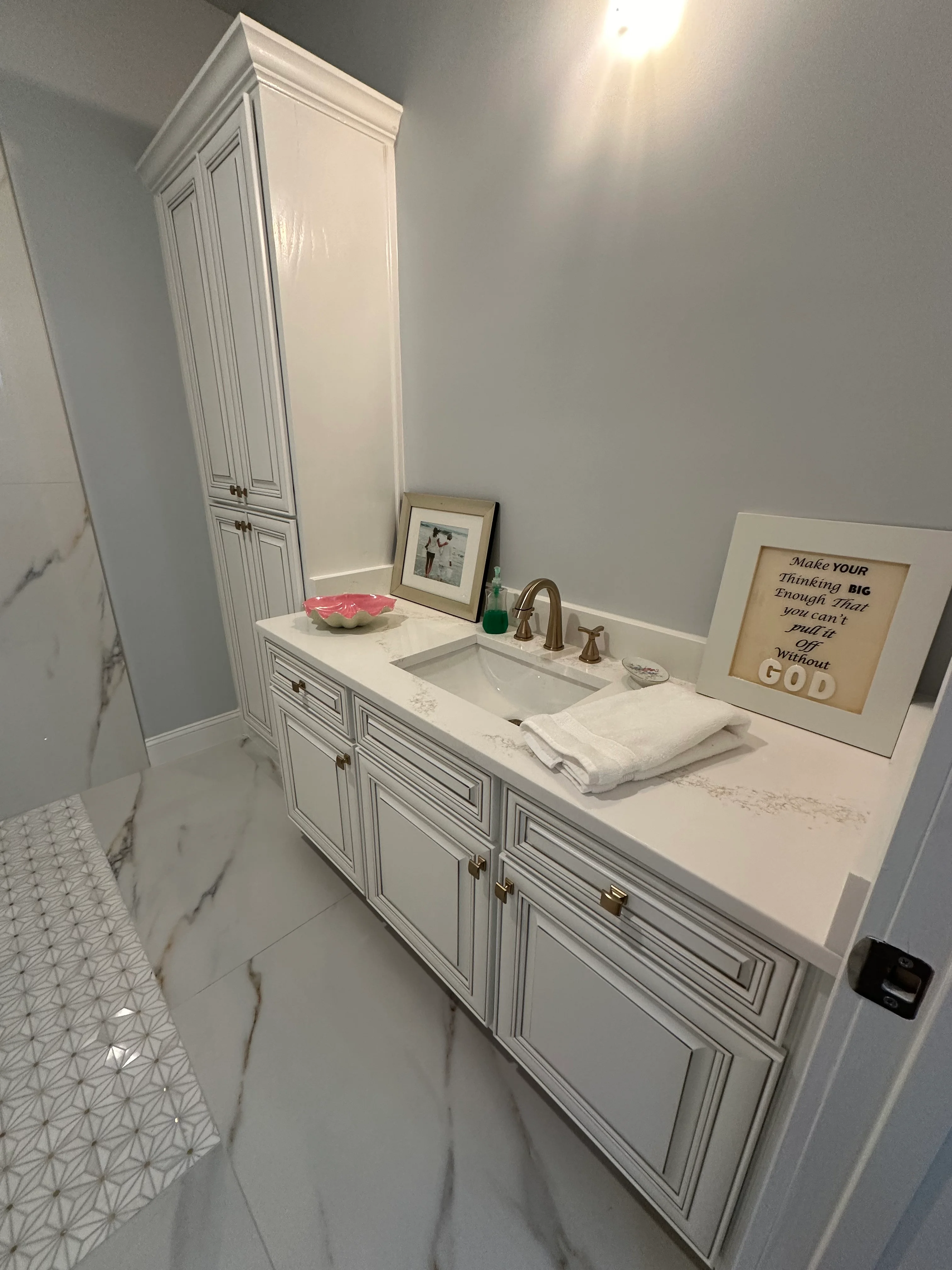 White bathroom vanity with marble countertop, integrated sink, and tall linen cabinet tower
