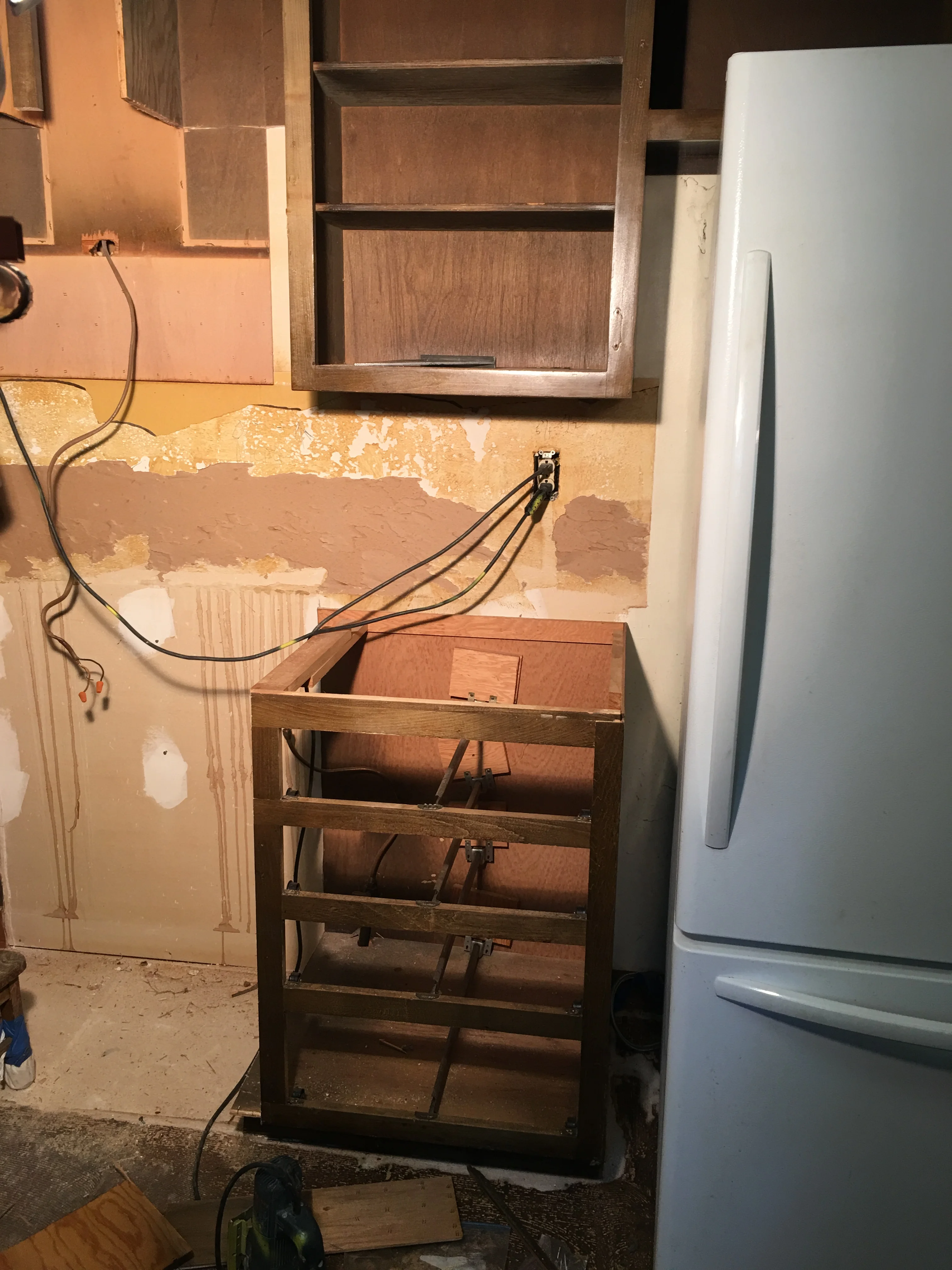 Wood kitchen cabinets under installation with electrical wiring and drywall prep work visible