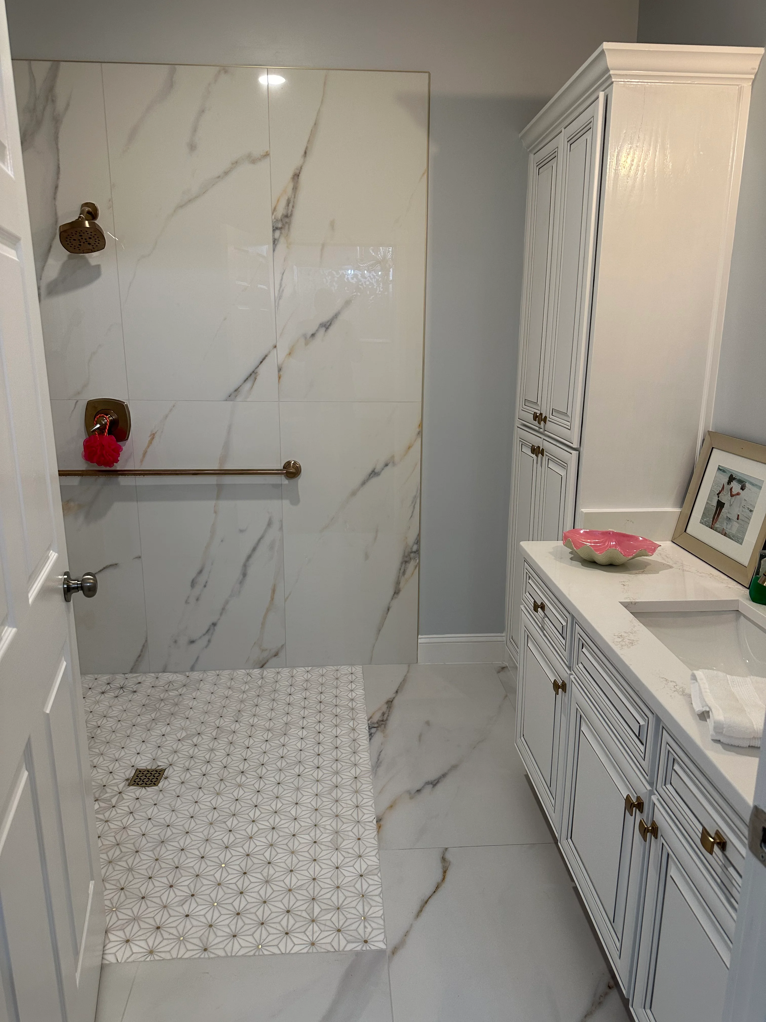 Modern bathroom with marble shower enclosure, white vanity cabinets, and geometric floor tile