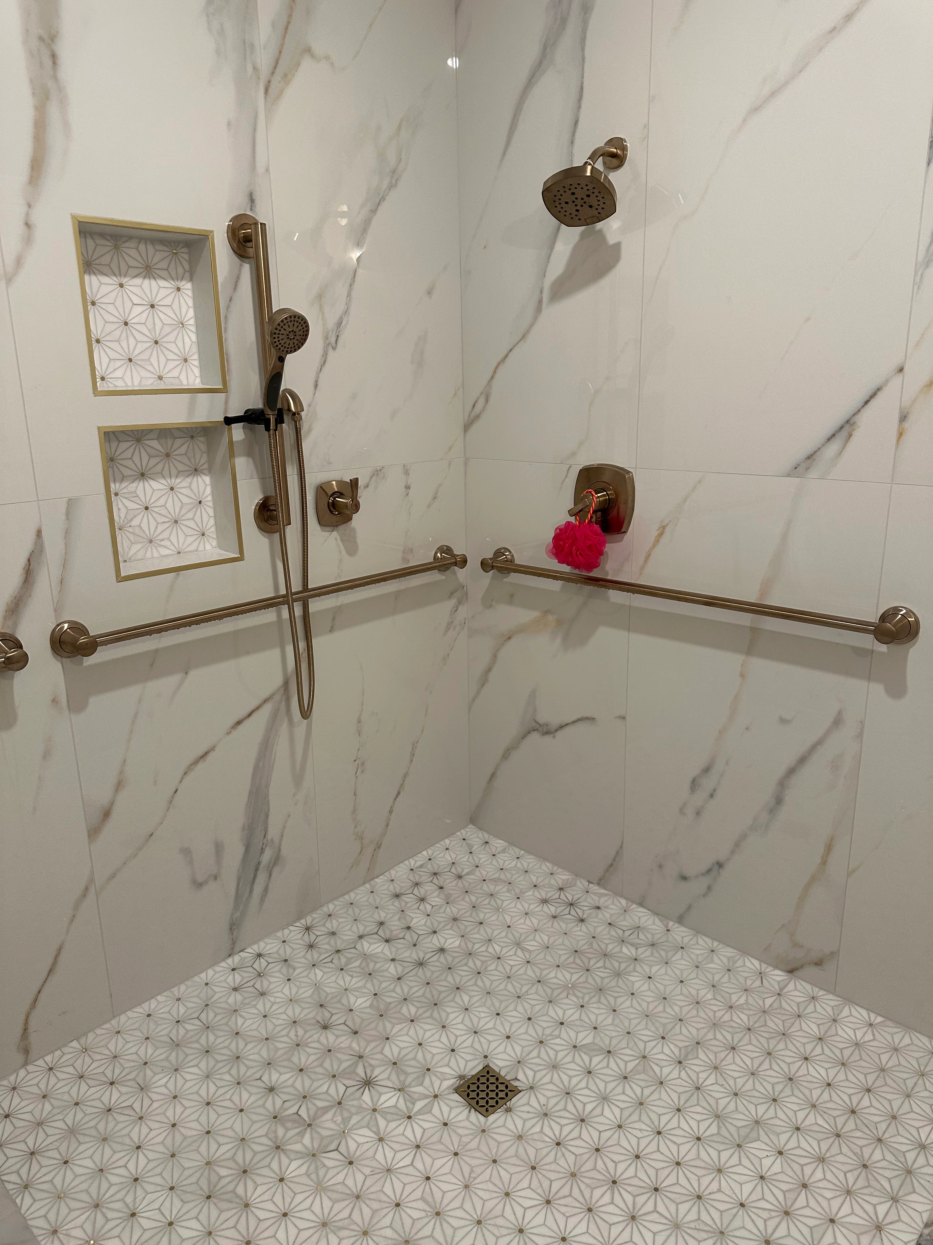 Modern shower with marble tile walls, geometric floor pattern, and brass fixtures